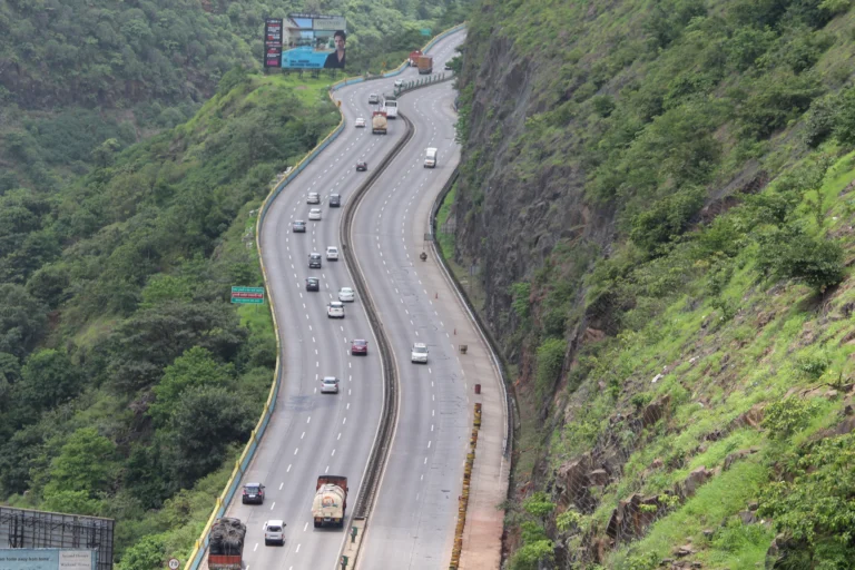 Aerial view of the winding Mumbai Pune Expressway passing through the green Lonavala mountains with moving traffic.